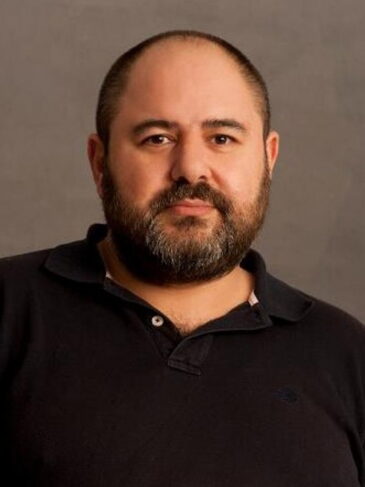 A middle-aged man with a beard wearing a black polo.
